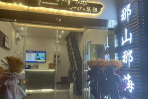 A hotel reception area with a digital display, a staircase, and a reception desk. - Here Nashan Nahai Surfing Seaview Homestay (Sanya Wuzhizhou Island Houhai Bay Branch) (Sanya)