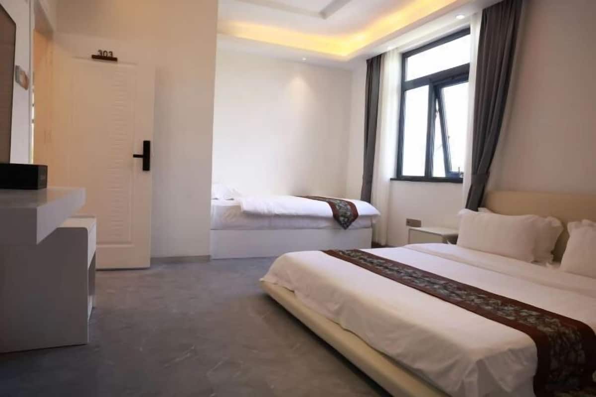 Une chambre d’hôtel avec un grand lit, un lit plus petit, un bureau et une fenêtre avec des rideaux.