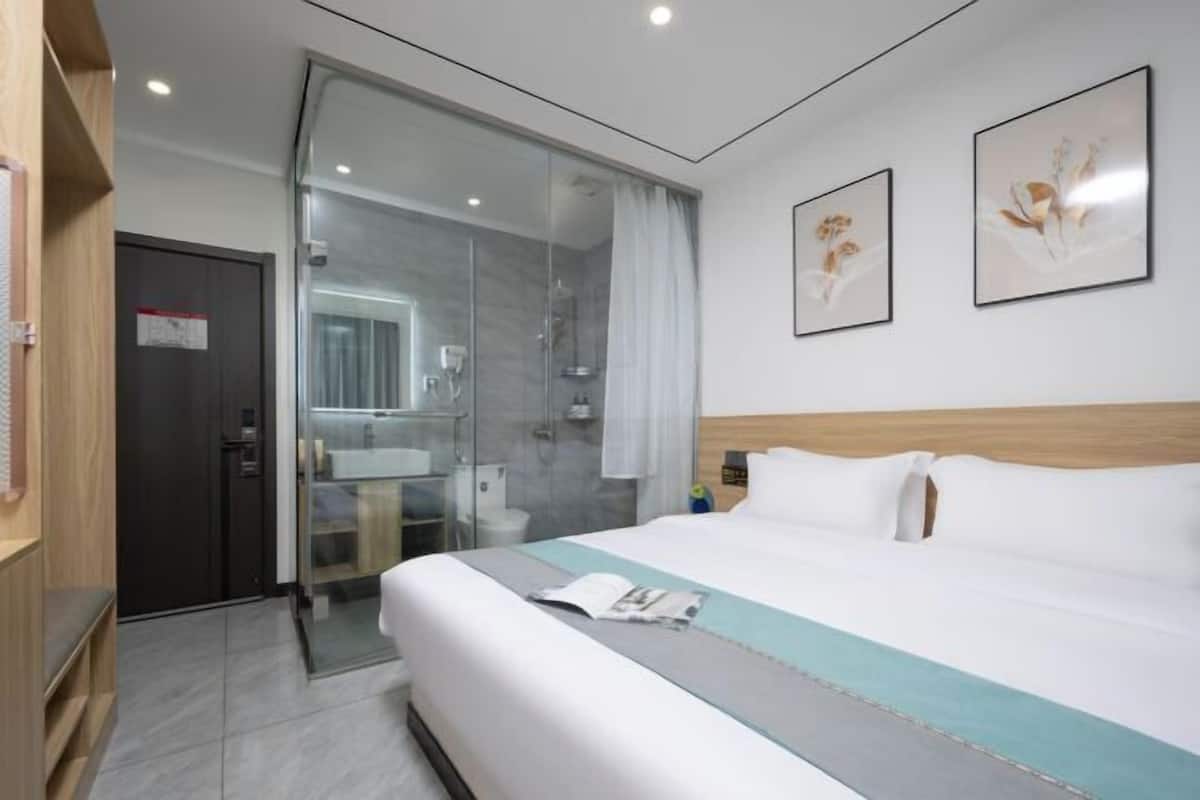 Une chambre d’hôtel moderne avec un grand lit, une douche en verre, une tête de lit en bois et deux œuvres d’art encadrées au mur.