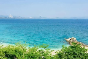Vista costiera con acqua blu cristallina, uno sperone roccioso e edifici in lontananza.