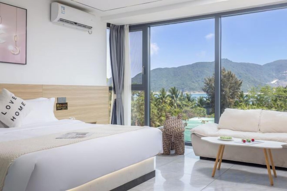Une chambre d’hôtel avec un grand lit, un canapé, une petite table et une vue sur les montagnes et la verdure.