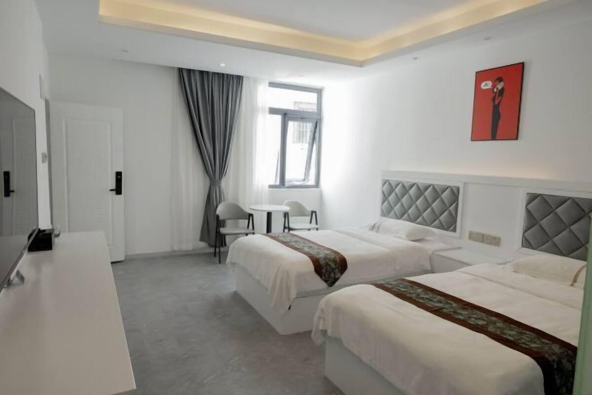 Une chambre d’hôtel avec deux lits, un bureau, une chaise, une petite table et une fenêtre avec des rideaux.