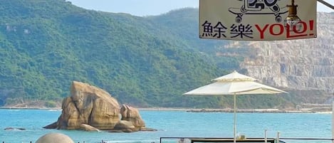 Eine Strandansicht mit einer großen Felsformation, einem Tisch mit Stühlen und einem Schild mit chinesischen Schriftzeichen.