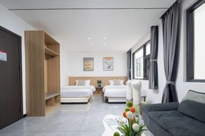 Quarto de hotel moderno com duas camas, um sofá, um guarda-roupa de madeira e uma pequena mesa com objetos decorativos.