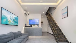 A modern hotel lobby with a grey sofa, a reception desk, a flat-screen TV, and a staircase. - Here Nashan Nahai Surfing Seaview Homestay (Sanya Wuzhizhou Island Houhai Bay Branch) (Sanya)