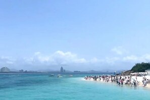 Une plage bondée, avec une eau calme et des bâtiments qui se dessinent à l’horizon.