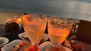 Two glasses of a clear beverage on a table with plates of food, set against a beach backdrop. - Here Nashan Nahai Surfing Seaview Homestay (Sanya Wuzhizhou Island Houhai Bay Branch) (Sanya)