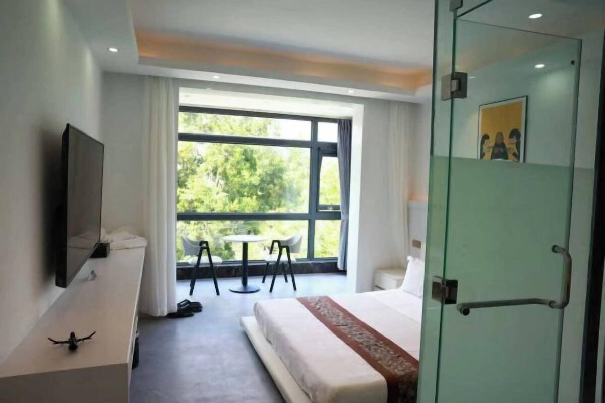 Une chambre d’hôtel avec un lit, une télévision, un balcon avec une table et des chaises, et une porte avec une poignée.