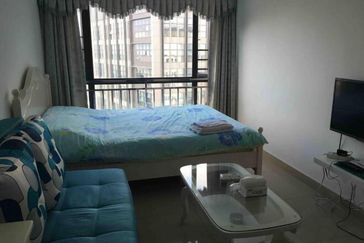 Ein Hotelzimmer mit Bett, Sofa, Glastisch, Fernseher und einem Fenster mit Vorhängen.