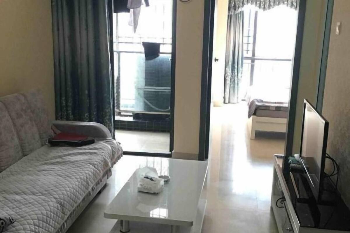 Ein Zimmer mit einem Bett, einem weißen Couchtisch, einem Fernseher und einer Schiebetür, die auf einen Balkon führt.