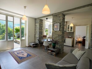A spacious living area with a stone accent wall, a gray sofa, a dining table with chairs, and a kitchen in the background.