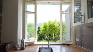 A kitchen with a large window, a sink, and wooden cabinets. - Pottery House (Carate Urio)