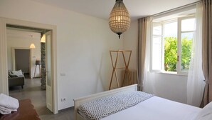 A bedroom with a bed, a standing lamp, a window with curtains, and a view of greenery outside. - Pottery House (Carate Urio)