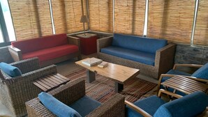 Un coin salon accueillant avec des meubles en osier et des coussins bleus, une table basse en bois et un canapé rouge.