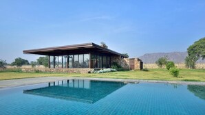 Un bâtiment moderne à la façade vitrée, doté d’une piscine et surplombant un paysage montagneux.
