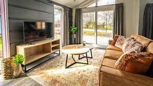 A modern living room with a large flat-screen TV, a wooden coffee table, and a leather sofa. - Modern Chalet in a Holiday Park, Bordering the Hoge Veluwe National Park (Arnhem)