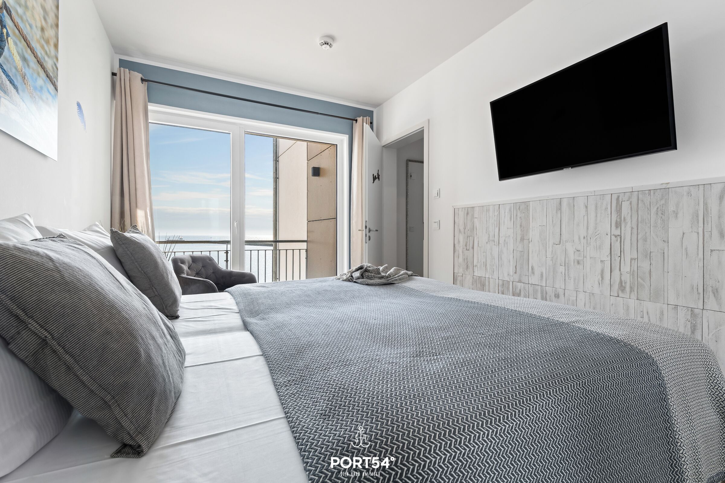 A modern bedroom with a large bed, a mounted TV, and a view of the outdoors.