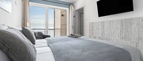 A modern bedroom with a large bed, a mounted TV, and a view of the outdoors.
