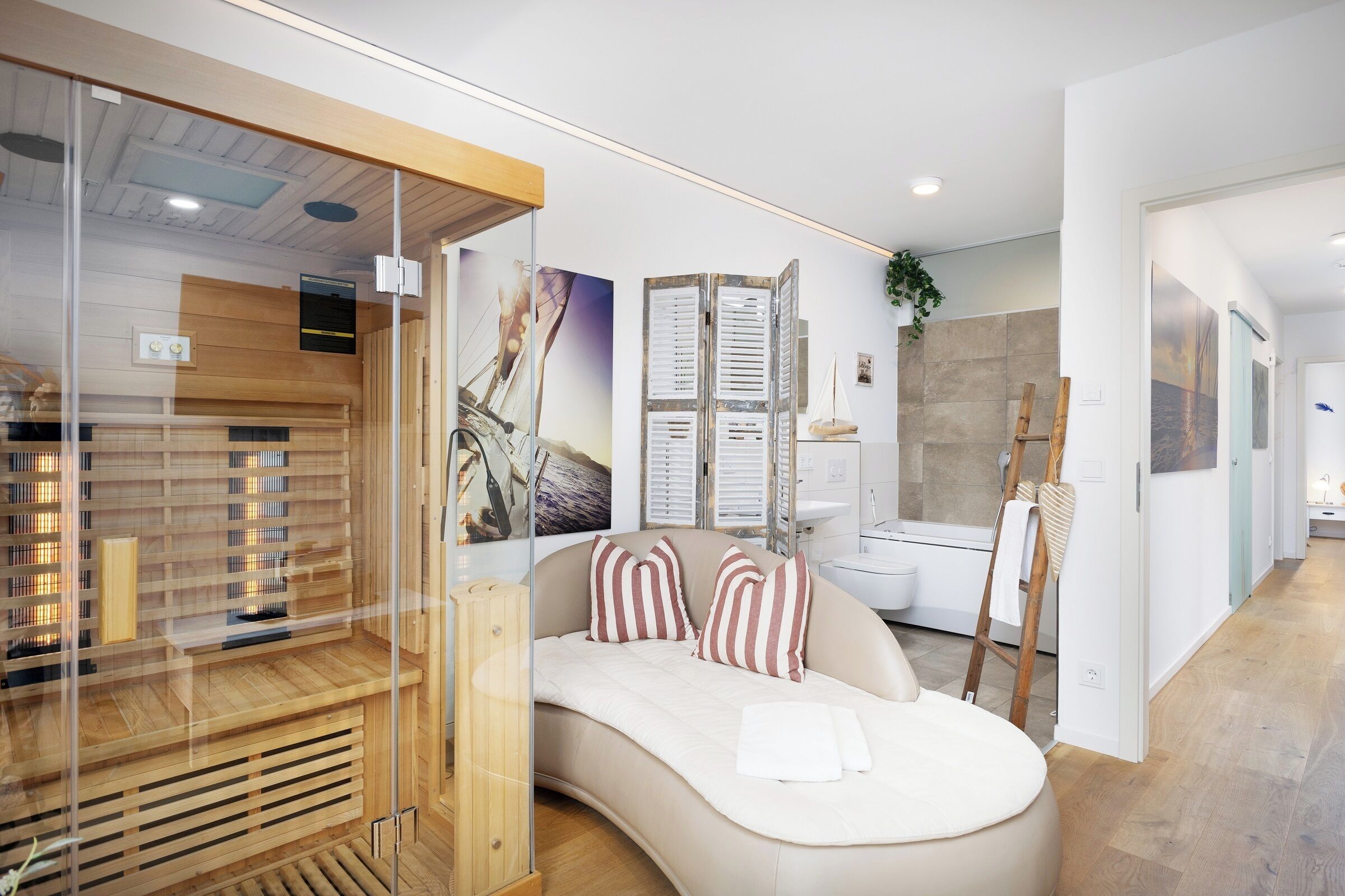 Une chambre à coucher moderne avec un lit aux lignes courbes, un espace clos en verre avec un intérieur en bois, et une salle de bain dotée d’une baignoire et d’une échelle en bois.