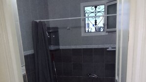 Une petite salle de bain compacte, équipée d’une douche, de toilettes et d’une fenêtre.