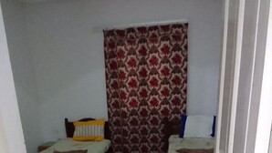 Une petite pièce avec deux lits simples, un rideau à motifs et une moquette rouge.