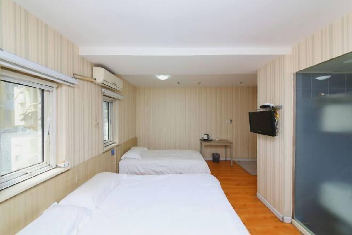 A hotel room with two beds, a desk, a TV, and a window.