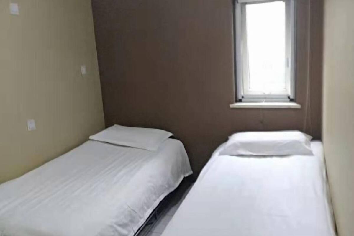 A small, single-room accommodation with two single beds, a window, and plain walls.