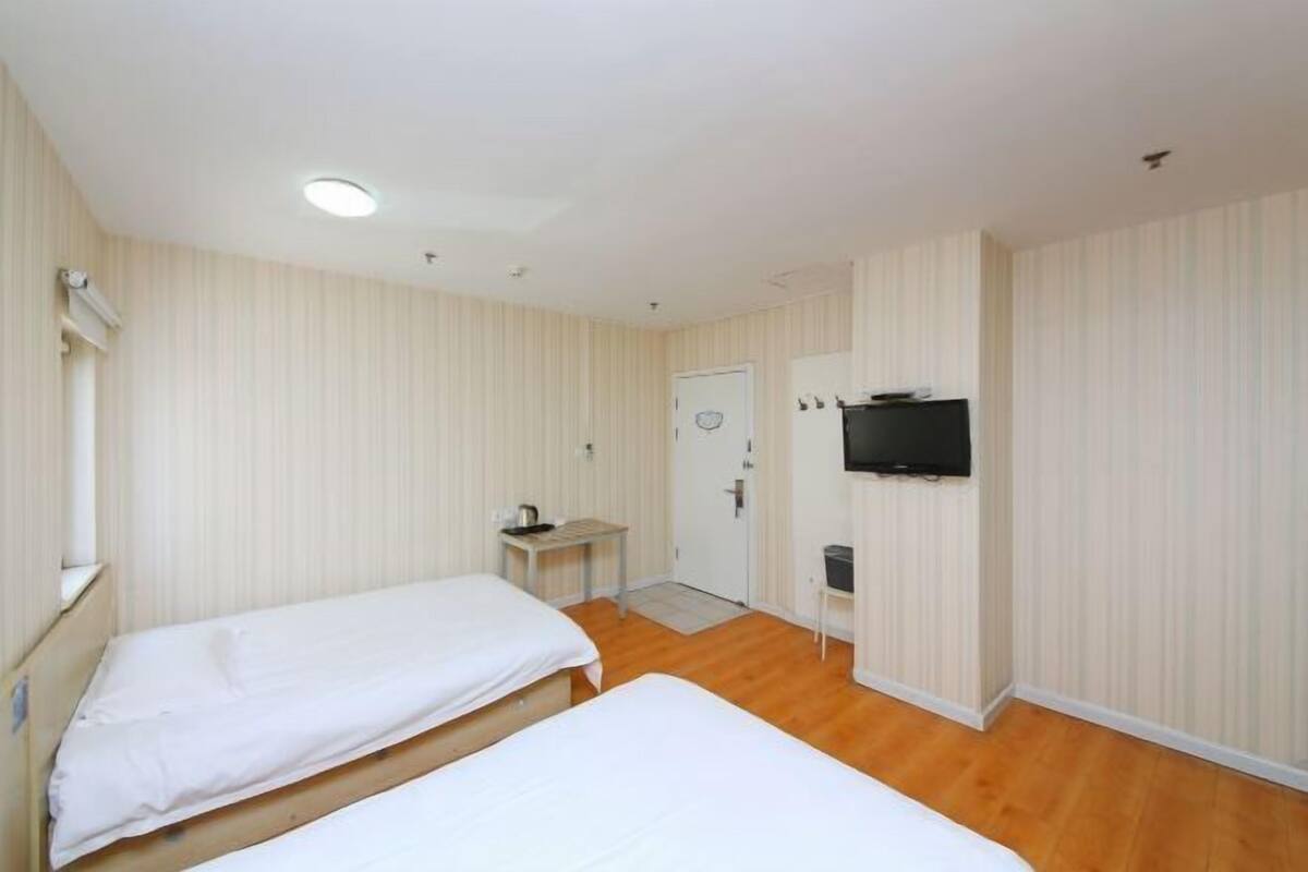 A room with two beds, a small table, a television, and a door.