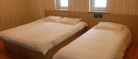 A room with two single beds, wooden flooring, and two windows with curtains.