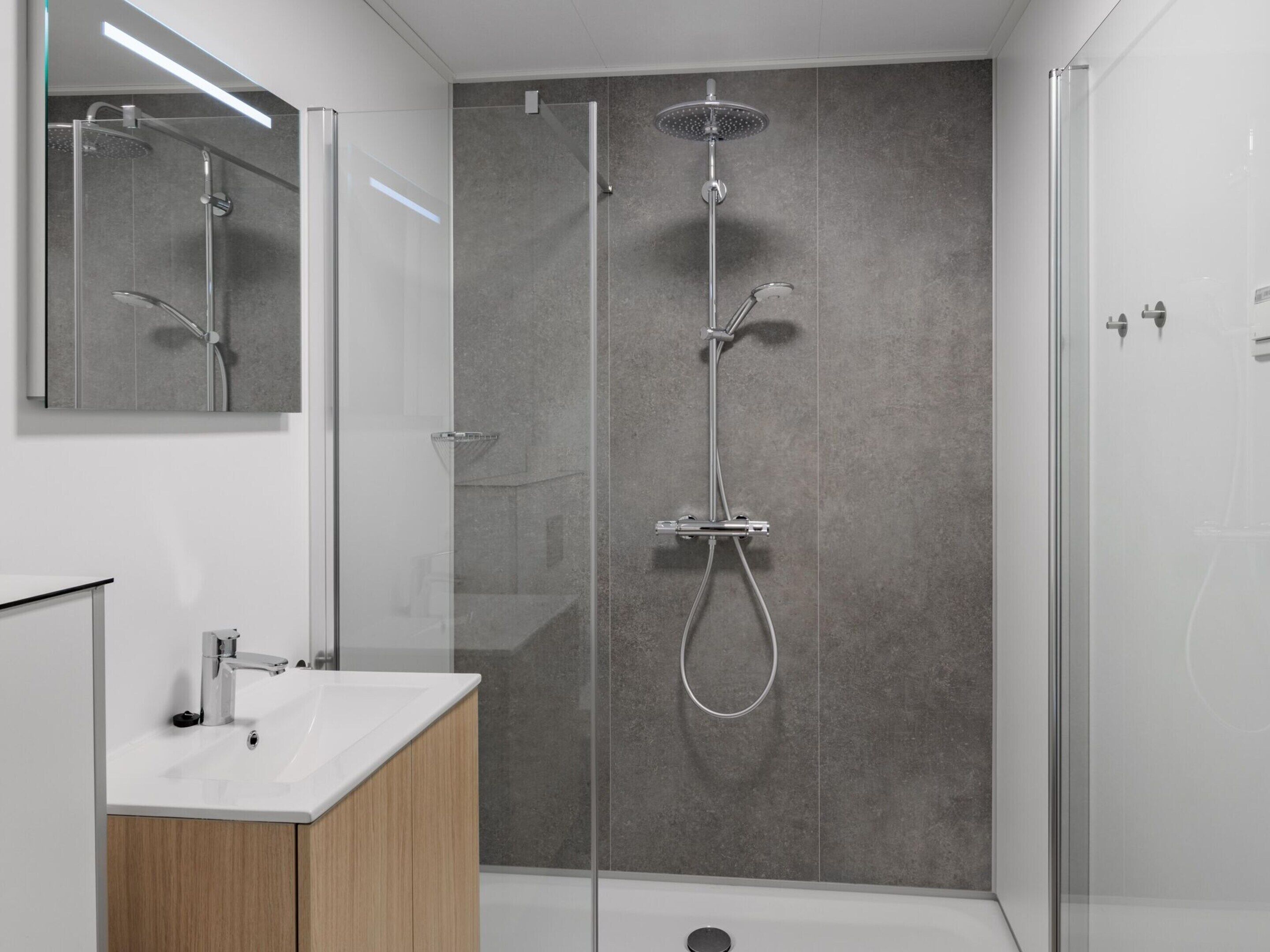 A modern bathroom with a glass-enclosed shower, a white sink, and a wooden cabinet.