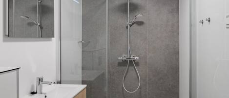 A modern bathroom with a glass-enclosed shower, a white sink, and a wooden cabinet.