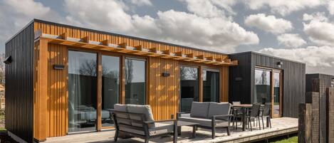 Ein modernes Haus mit einer Holzdielen-Terrasse, Sitzgelegenheiten im Freien und großen Schiebeg lass-Türen.