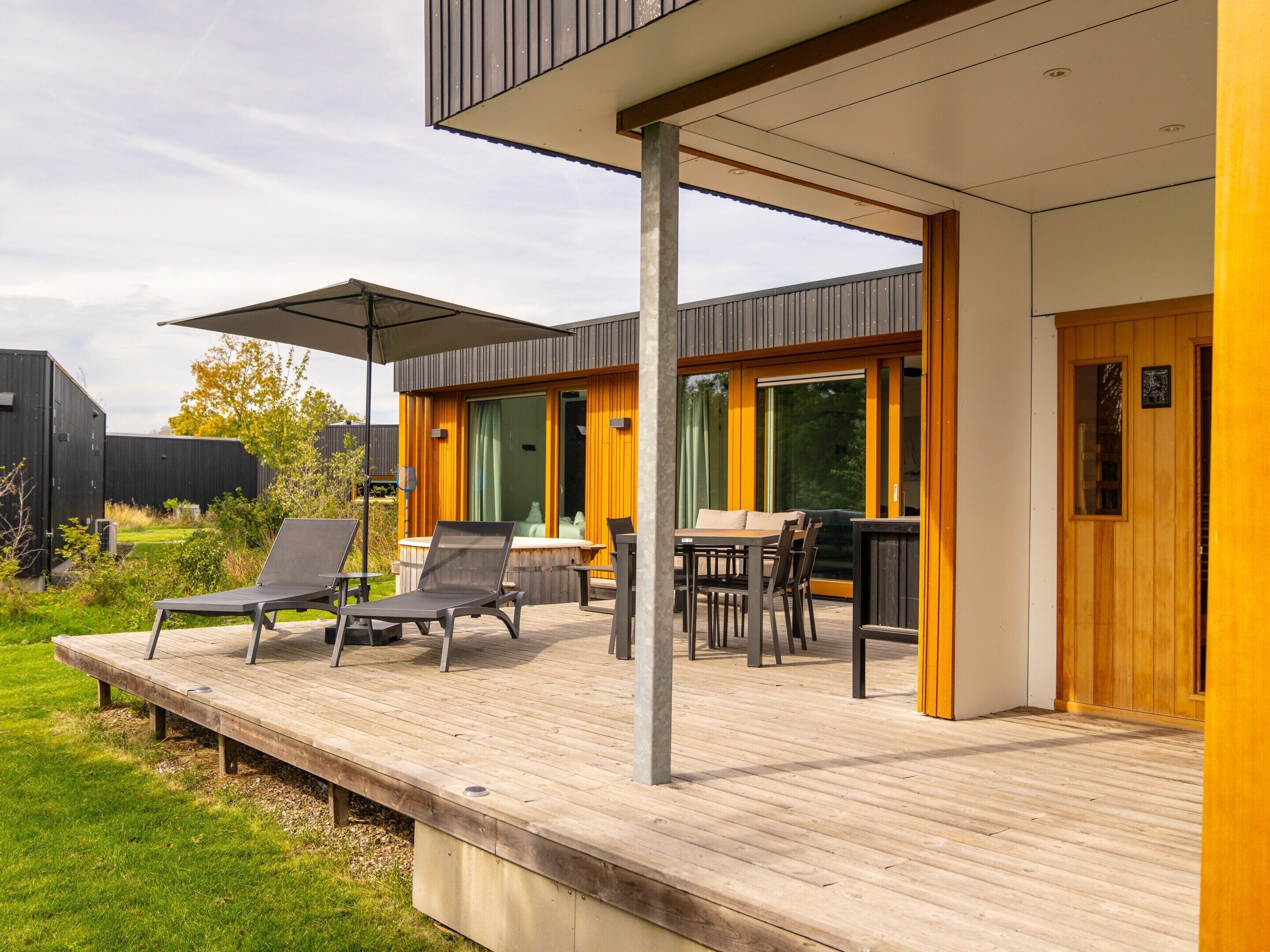 A modern outdoor deck with lounge chairs and a table, surrounded by wooden walls and large windows.