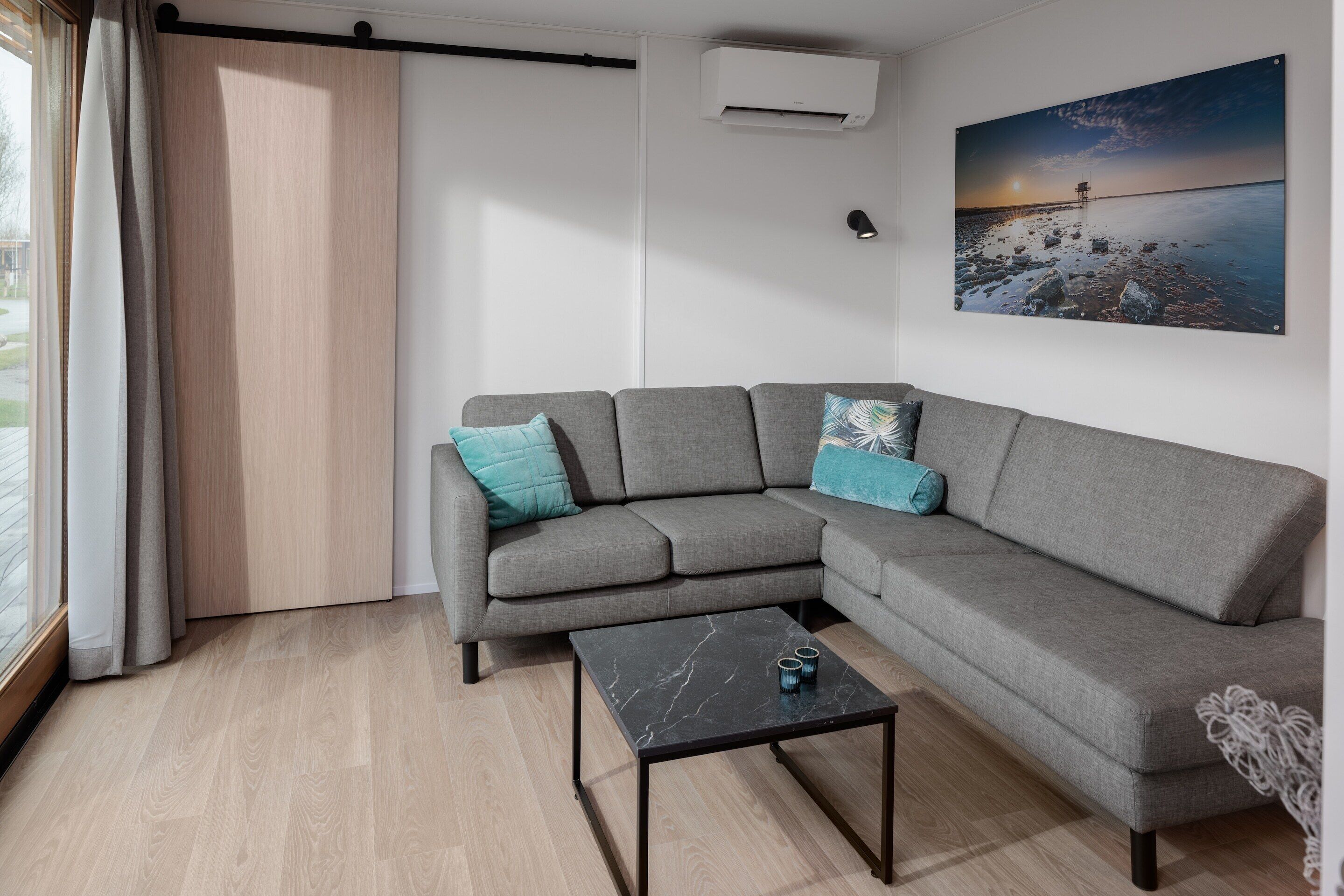 Ein modernes Wohnzimmer mit einem grauen Ecksofa, einem Couchtisch aus schwarzem Marmor und einem großen Landschaftsbild an der Wand.