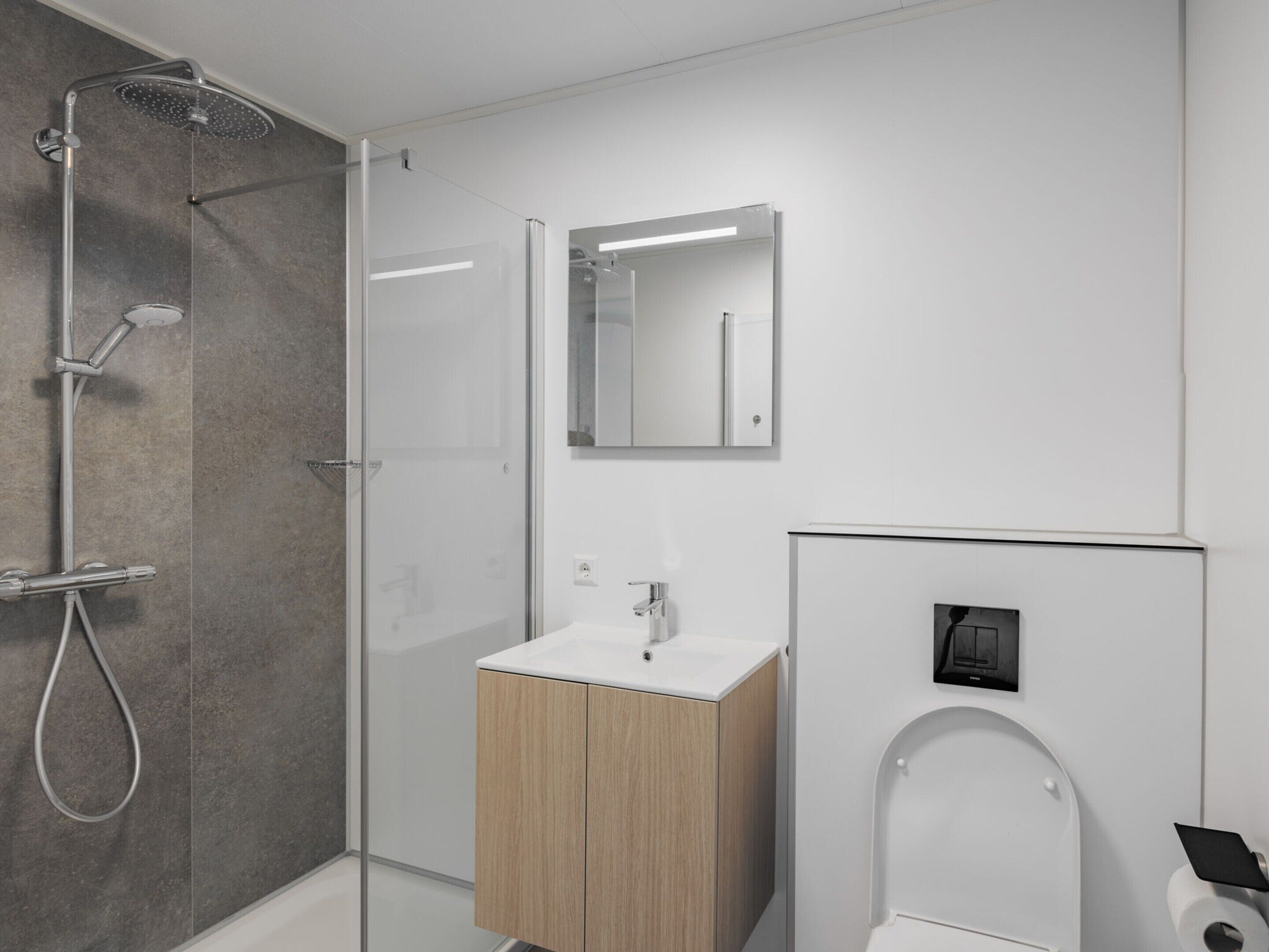 A modern bathroom with a glass-enclosed shower, a wooden vanity, a toilet with a bidet attachment, and a mirror above the vanity.