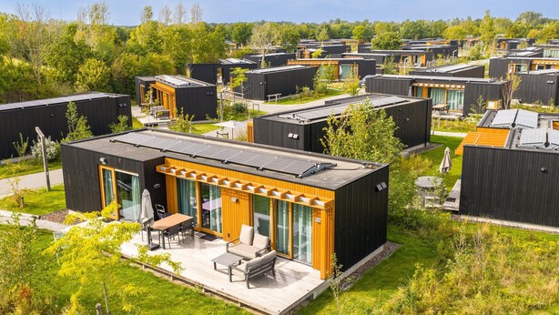 Een moderne woonwijk met compacte, donkere huizen, grote ramen en zonnepanelen.