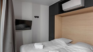 Een hotelkamer met een bed, een aan de muur bevestigde televisie en een airconditioning boven het bed.