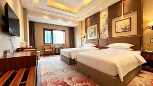 Ein Hotelzimmer mit einem großen Bett, zwei Nachttischen, einem Schreibtisch, einem Sessel und einem Fenster.