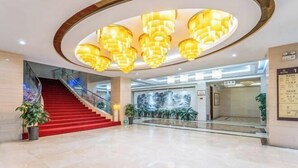 Eine großzügige Lobby mit einem roten Teppich und einer Wendeltreppe, darüber ein großer, runder Kronleuchter und eine Wand mit einem Wandgemälde.