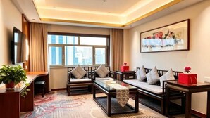 Ein Hotelzimmer mit einer Couch, Sesseln, einem Couchtisch, einem Fernseher, einem Schreibtisch und einem großen Fenster.