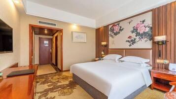 Een hotelkamer met een bed, nachtkastje, televisie en een bloemistisch kunstwerk aan de muur.
