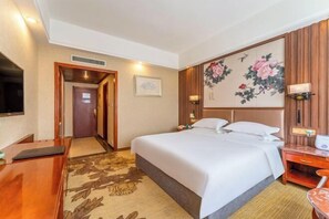 A hotel room with a bed, bedside table, TV, and a floral artwork on the wall. - Mudan Hotel (Heze)