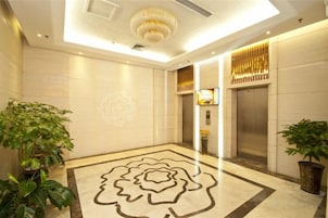 Vestíbulo de hotel con diseño moderno, que presenta una alfombra floral grande, un candelabro y un mostrador de recepción.