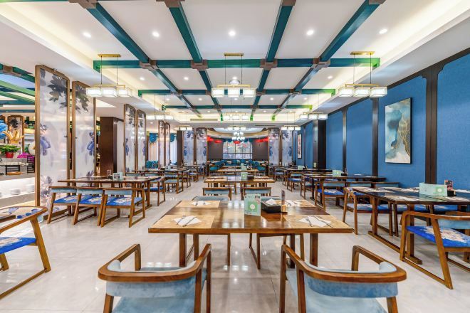Un restaurante espacioso con numerosas mesas y sillas, techo alto con vigas a la vista, y obras de arte en las paredes.