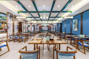 A spacious restaurant with multiple tables and chairs, a high ceiling with exposed beams, and artwork on the walls. - Mudan Hotel (Heze)