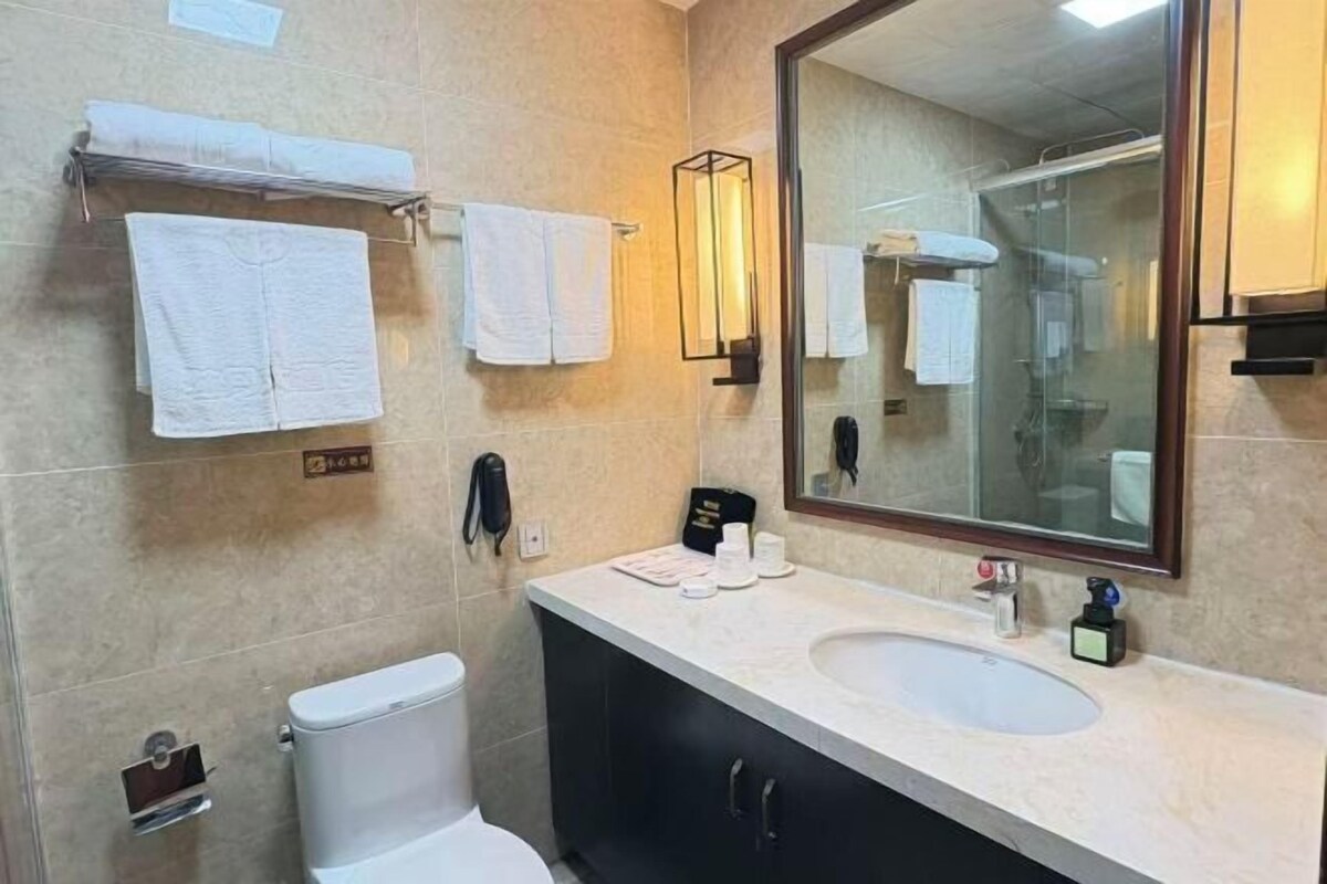 A bathroom with a toilet, sink, mirror, and towels on a rack.