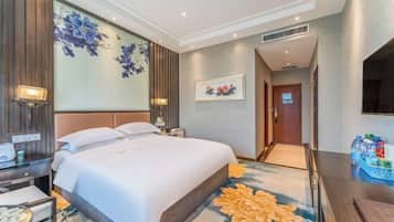 Una habitación de hotel con una cama grande, un escritorio con lámpara y un televisor montado en la pared.