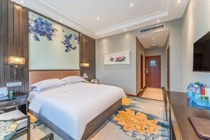 A hotel room with a large bed, a desk with a lamp, and a wall-mounted TV. - Mudan Hotel (Heze)
