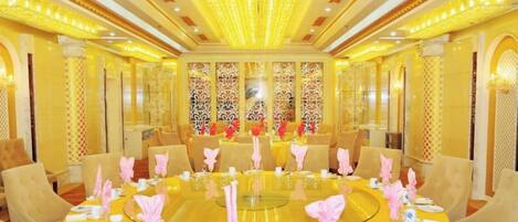 Mesa redonda dispuesta para una comida, con sillas alrededor, en una habitación con decoración elaborada y candelabros.