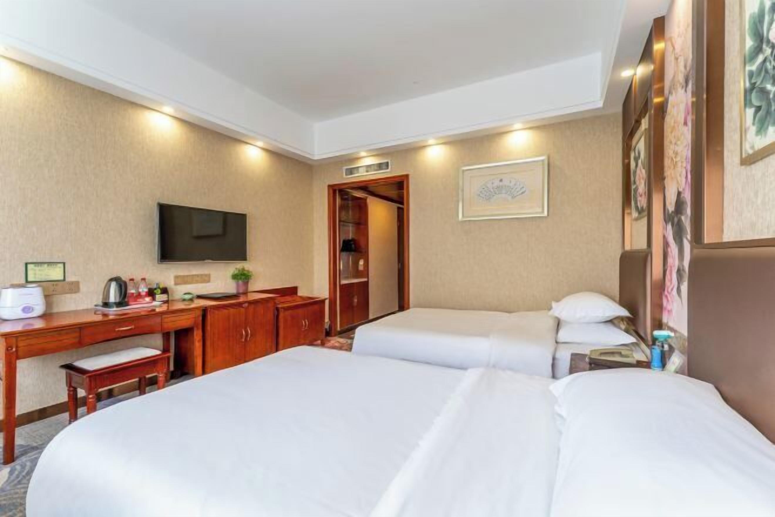 Habitación de hotel con dos camas, un escritorio con silla, televisión y puerta que da a un baño.